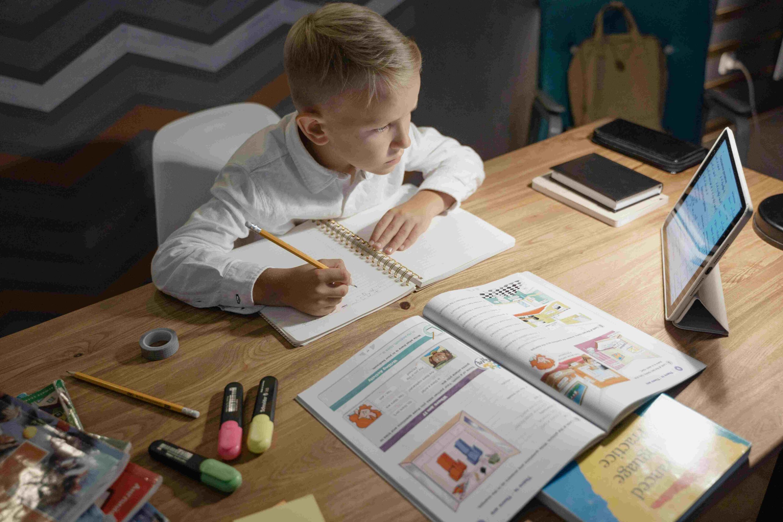 A young boy studying hard and taking notes with his ipad open.