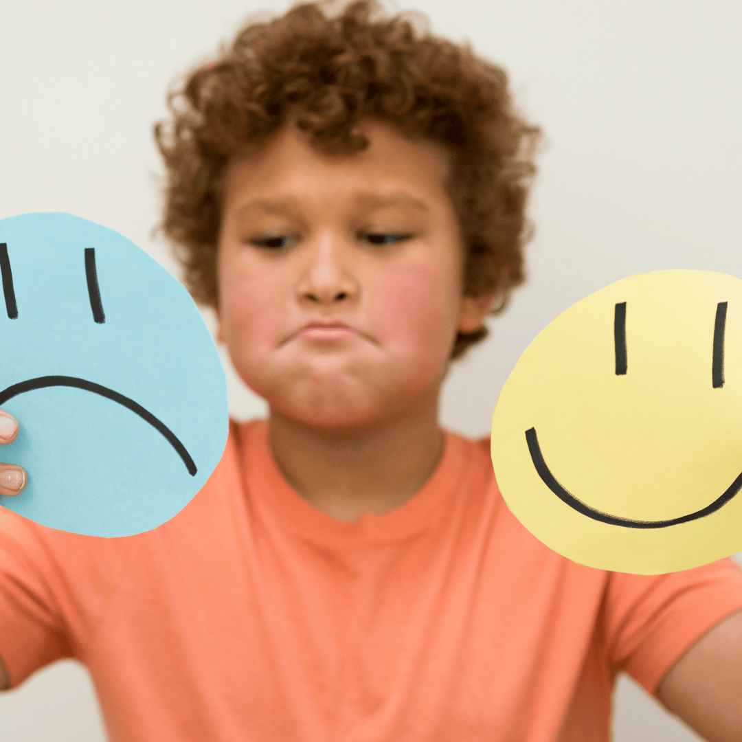 A young boy learning emotions with smily face and sad face card.