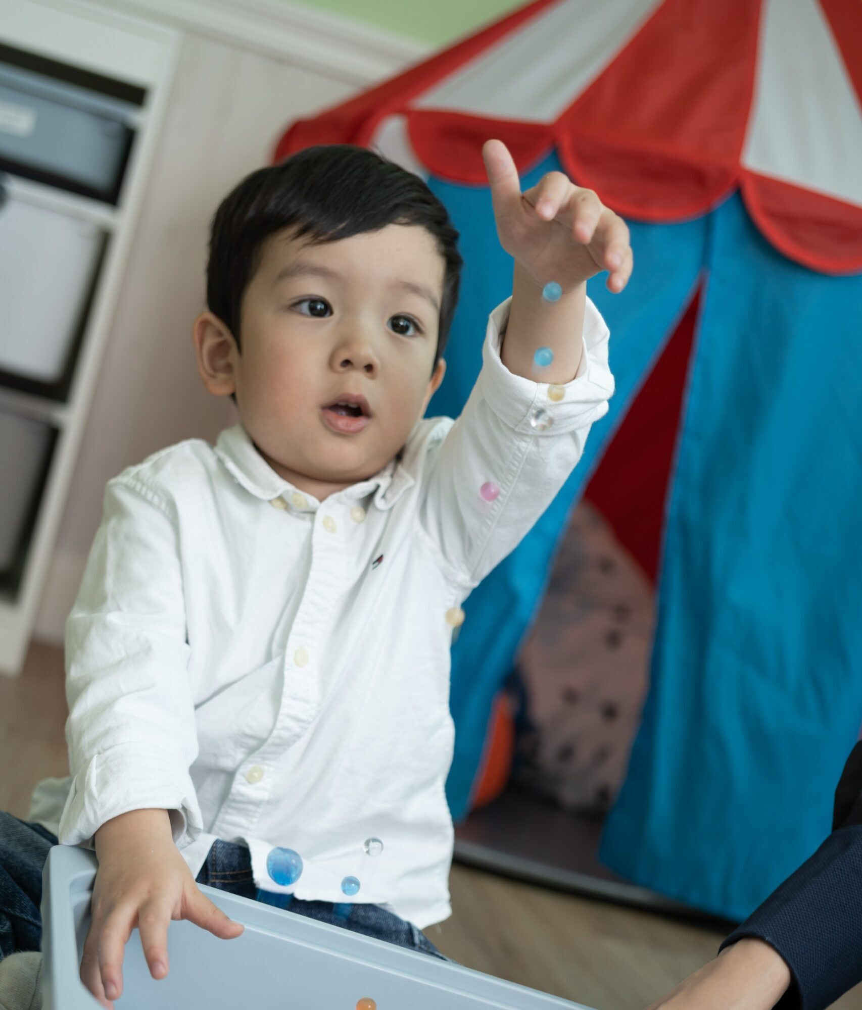 3 year old boy playing with sensory tray with colourful mini water beads and ping pong balls with BCBA certified Behavioural therapist in Sprout in Motion Wong Chuk Hang centre