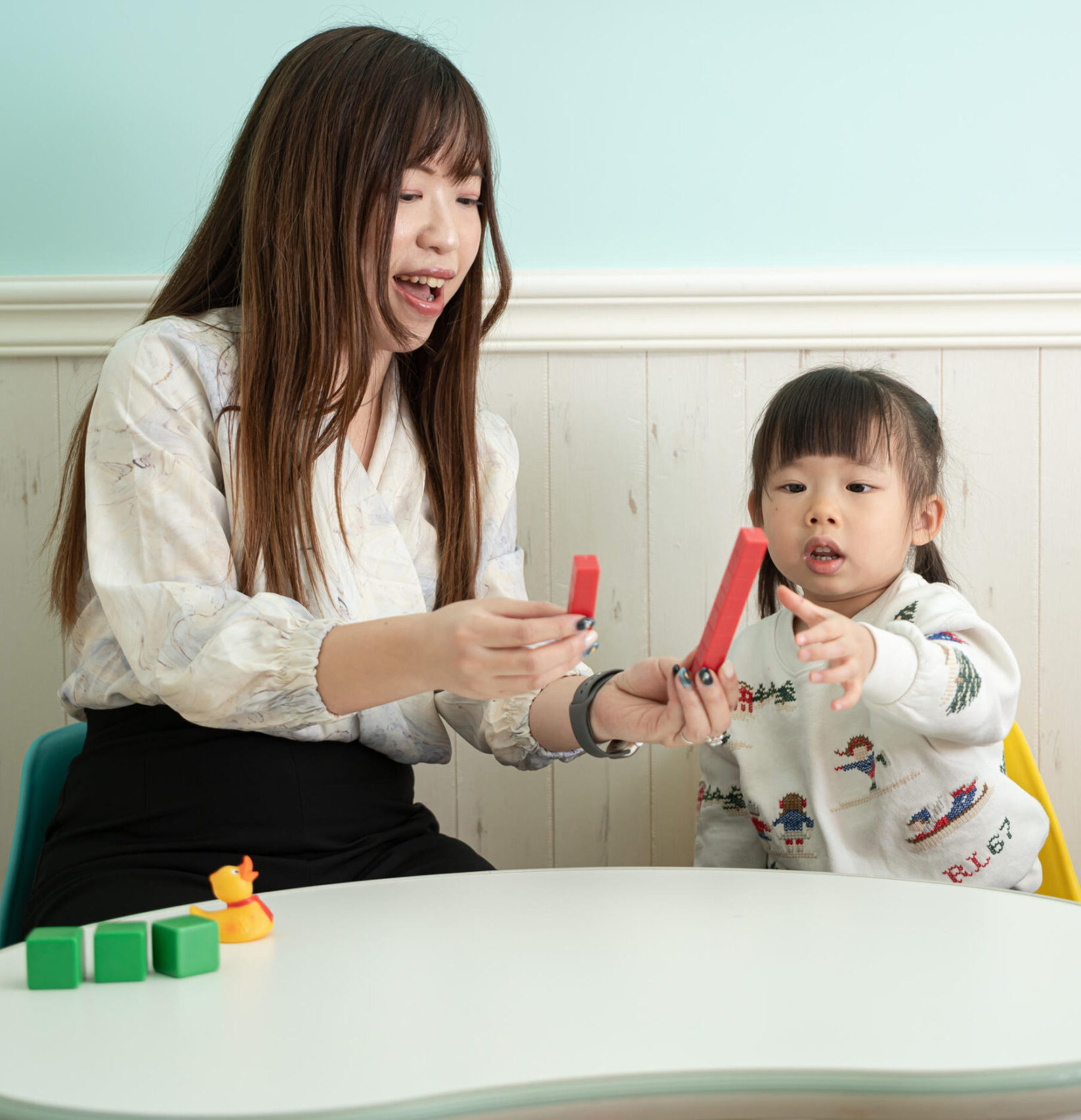Education Psychologist Ms Winkie with a 3 years old girl conducting developmental assessment with counting red, green and yellow blocks.