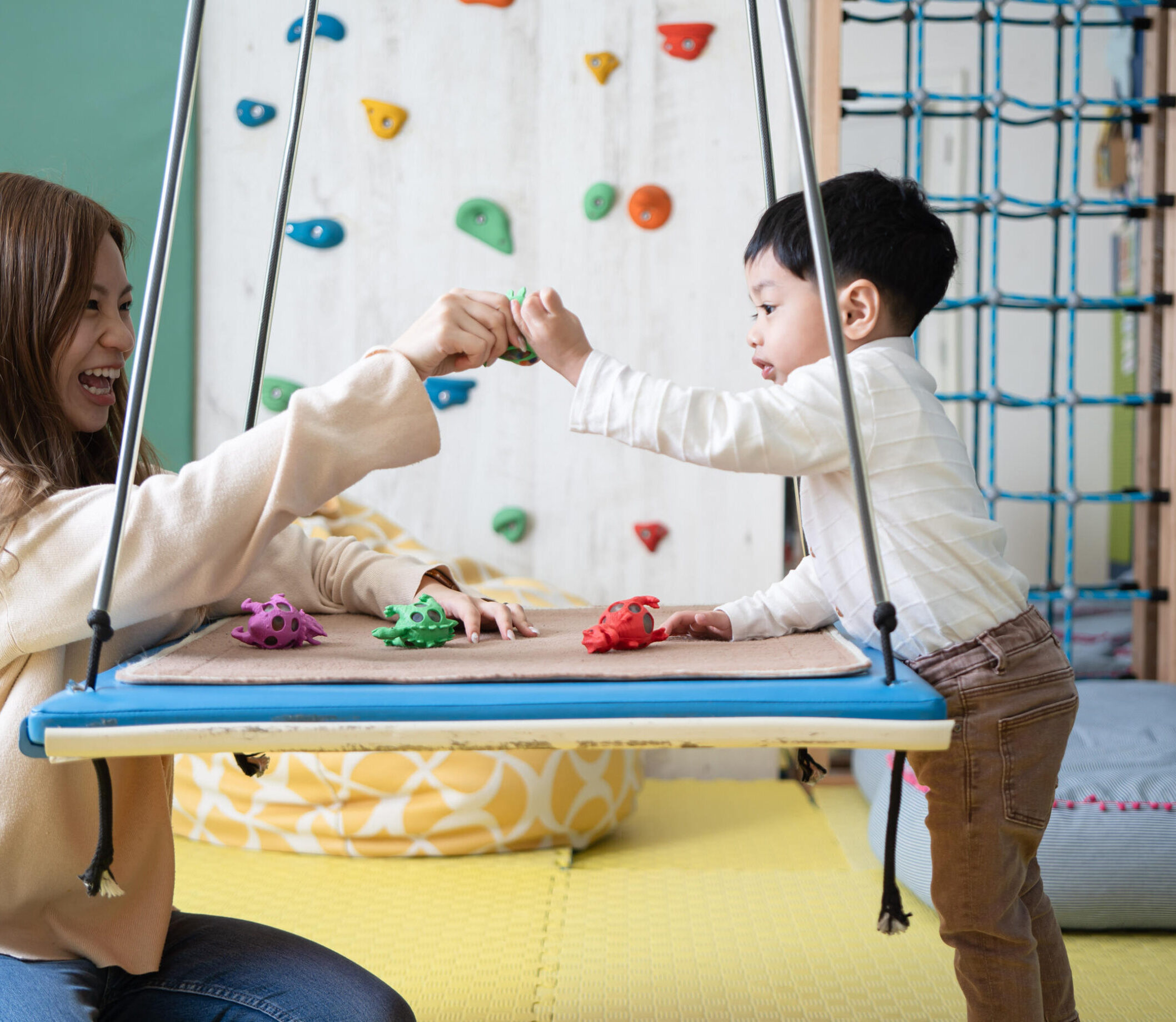 Ms Dorothy Cheung - OT therapist and a 5 years old boy happily playing with a red, green and purple dinosaur in Sprout in Motion Wong Chuk Hang OT room.